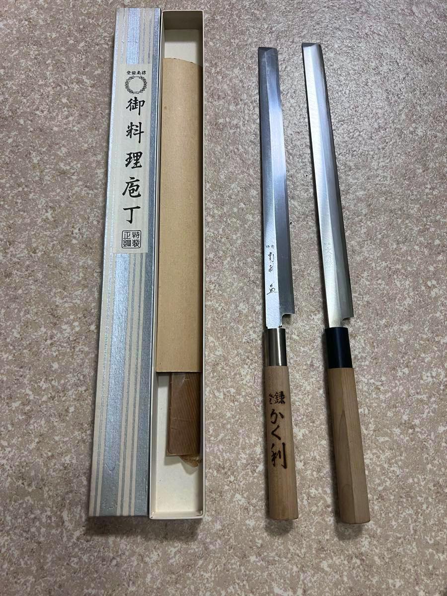Two Japanese sashimi/chef knives with wooden handles laid next to an open presentation box on a textured surface.