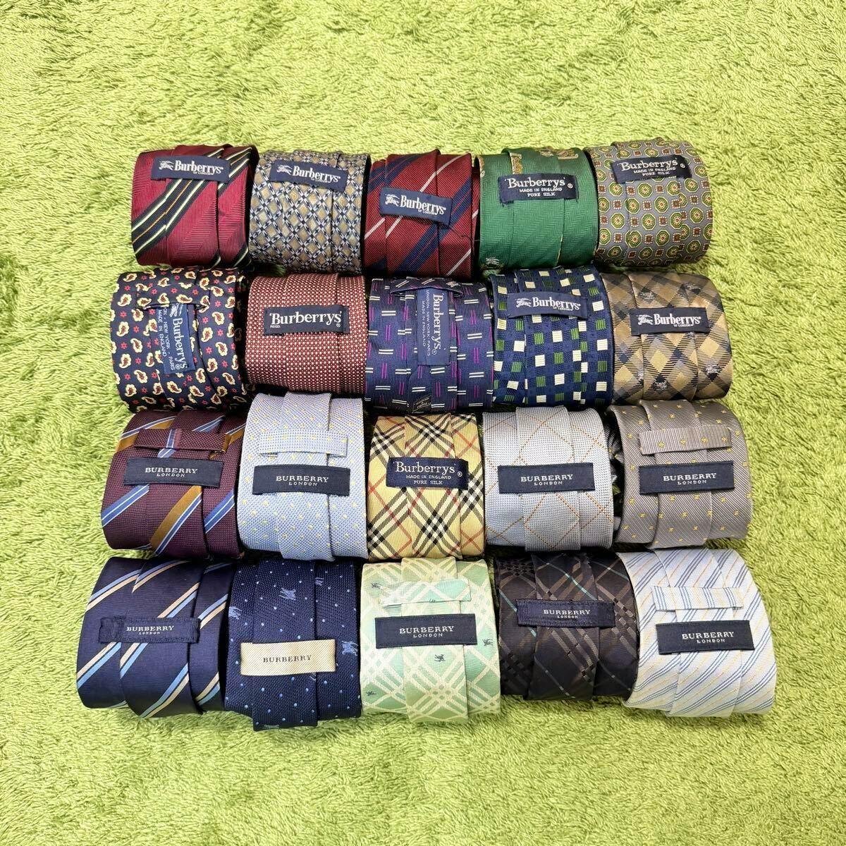 Twenty rolled silk Burberry neckties arranged in rows on a green textured surface, showing brand labels and various patterns.