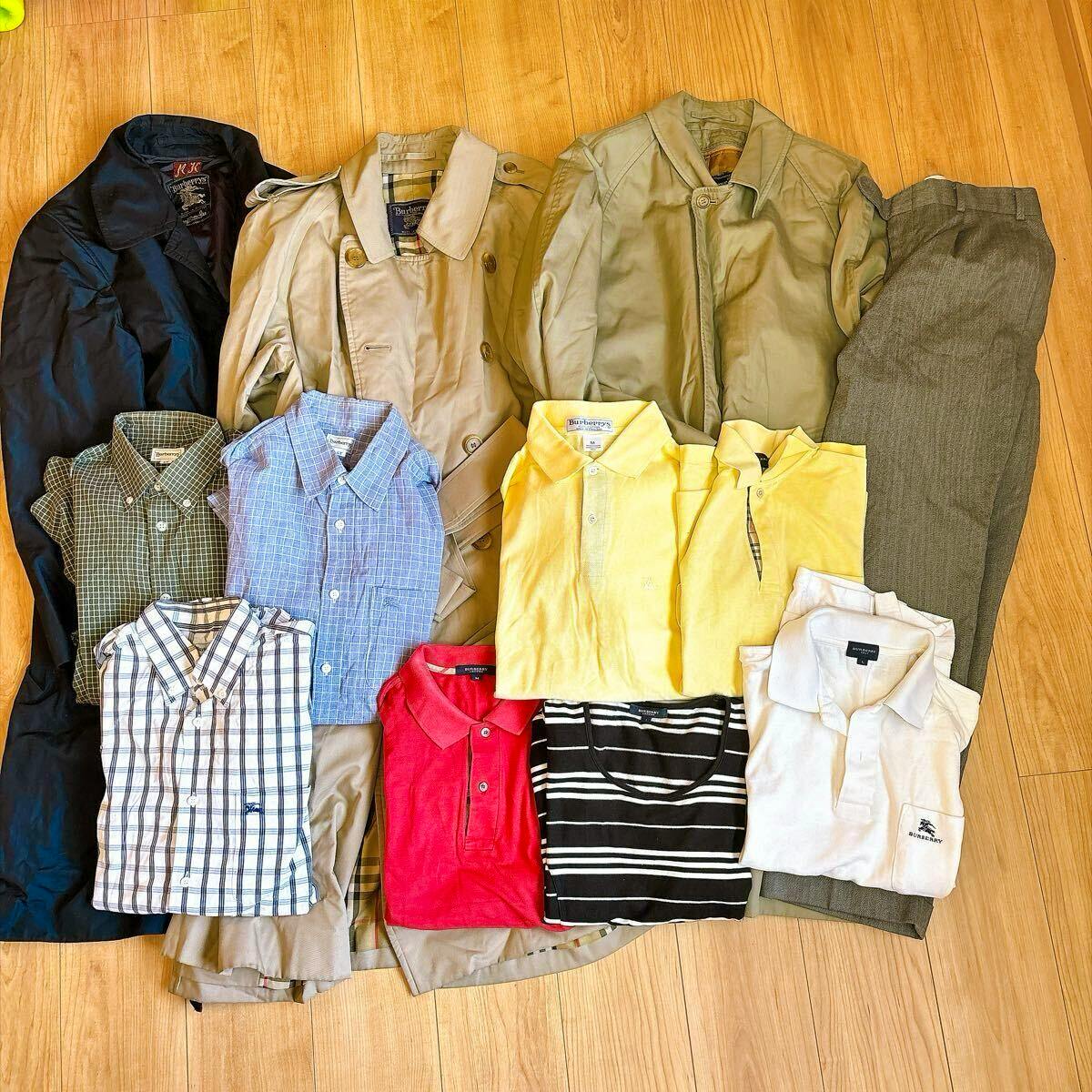 A laid-out assortment of Burberry trench coats, shirts, polo shirts, and trousers arranged on a wooden floor.