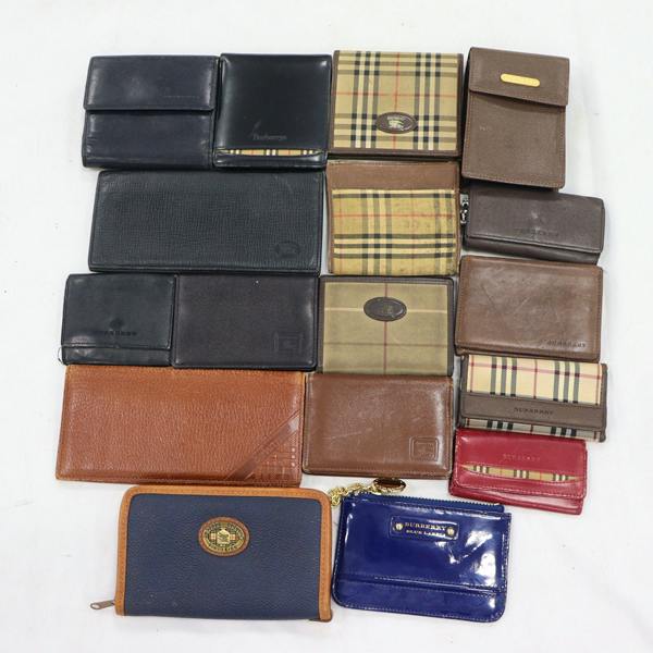 A laid-out group of wallets and small leather accessories, including Burberry-patterned wallets, on a white background.