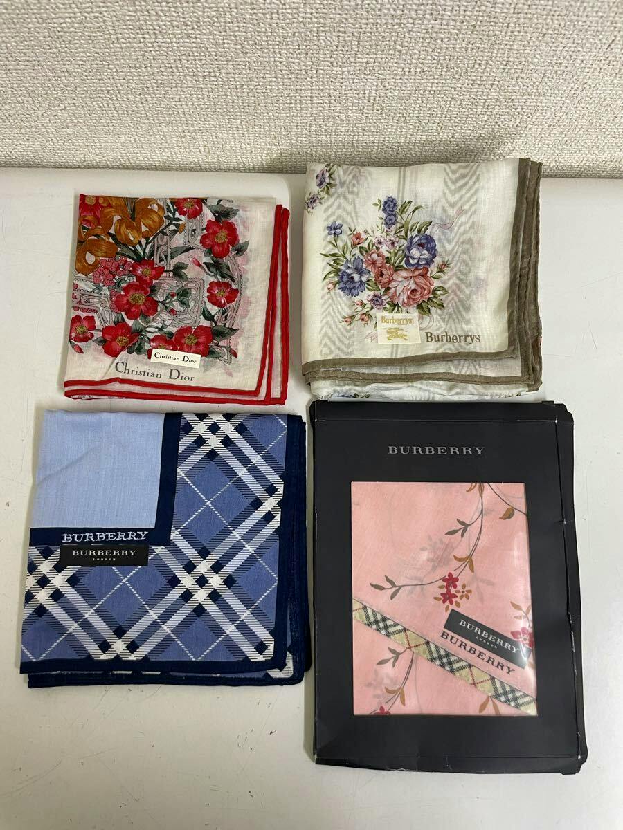 Four folded handkerchiefs on a white surface, including floral Christian Dior and Burberry designs and a boxed Burberry handkerchief.