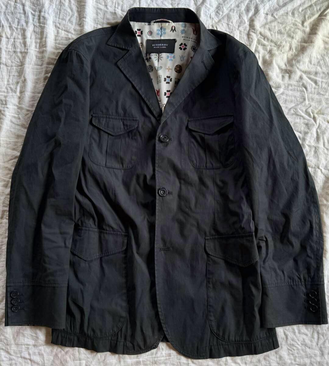 Black men's jacket laid flat showing the front with flap pockets, buttons, and patterned lining visible at the collar.