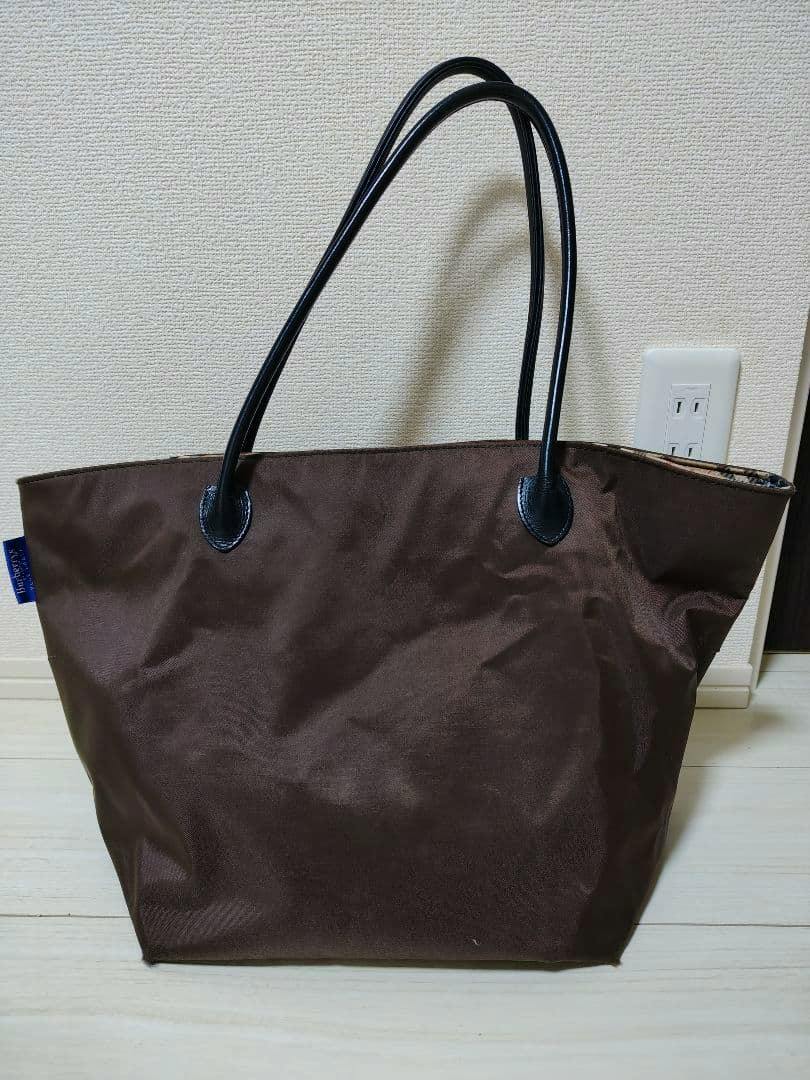 Dark brown canvas tote bag with black handles standing against a wall.