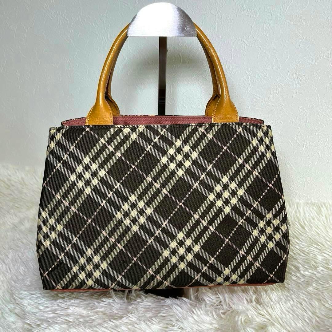 Front view of the checked nylon handbag with tan leather handles placed on a white fuzzy surface.