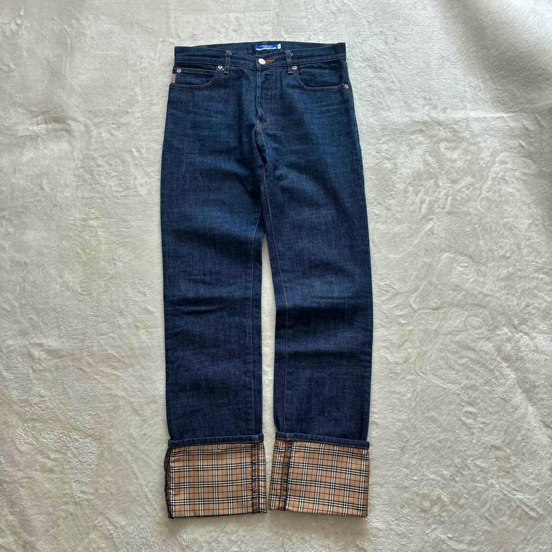 Men's straight dark blue denim jeans laid flat showing folded cuffs with Burberry Nova check pattern.