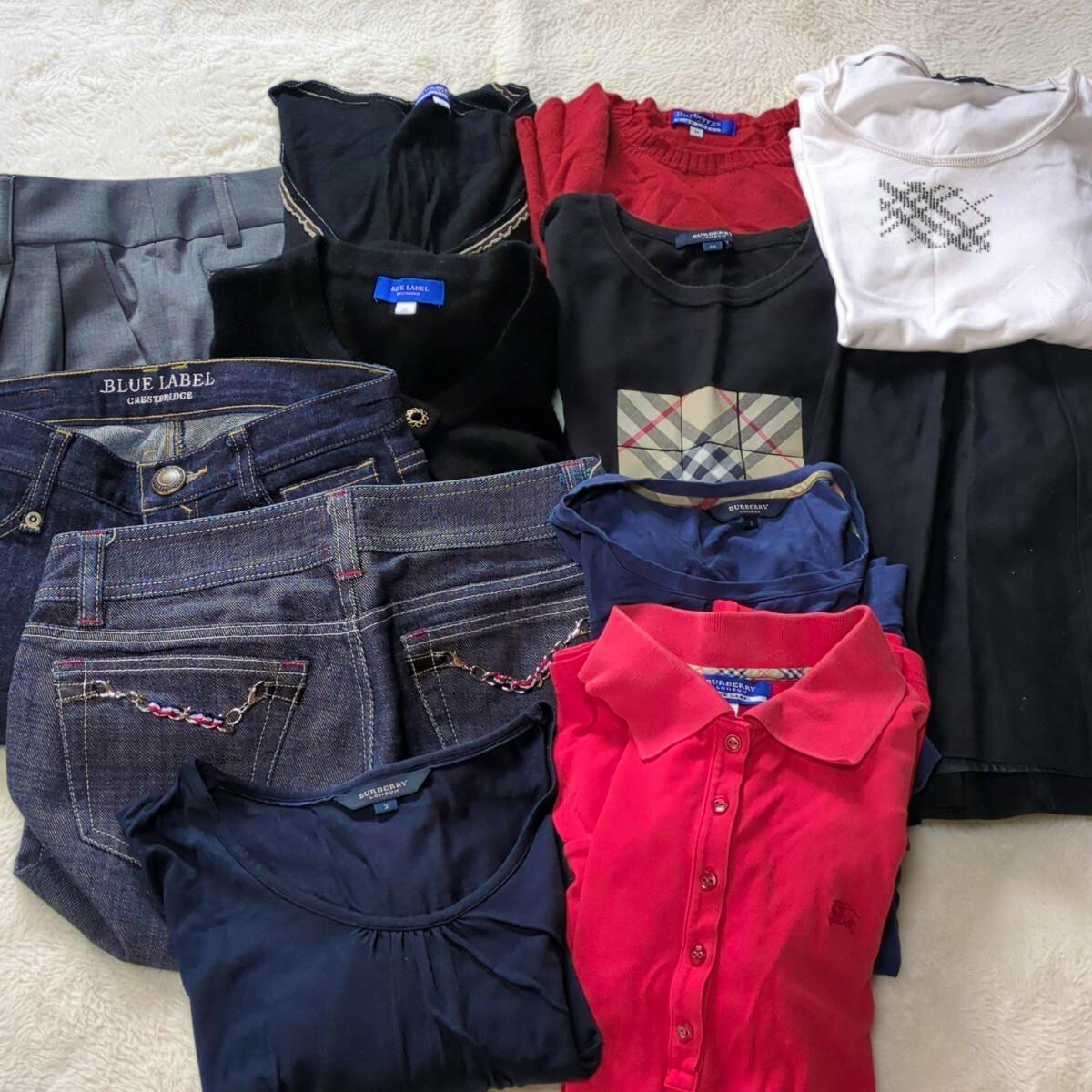 Flat lay of folded Burberry Blue Label clothing items including denim pants, skirts, and several tops on a light surface.
