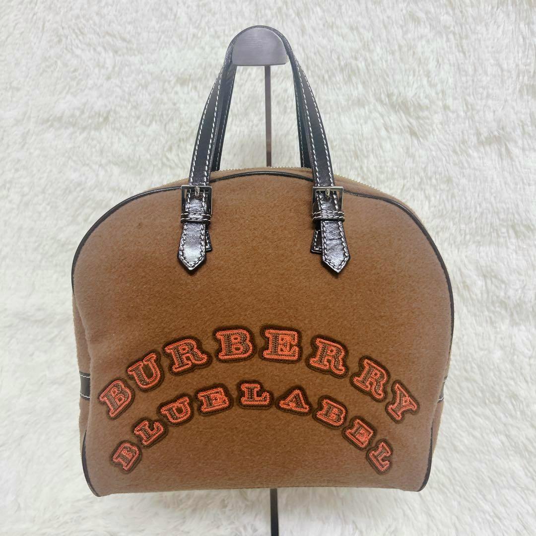 Front view of a brown Burberry Blue Label mini boston bag in wool with embroidered BURBERRY BLUE LABEL lettering and black handles.