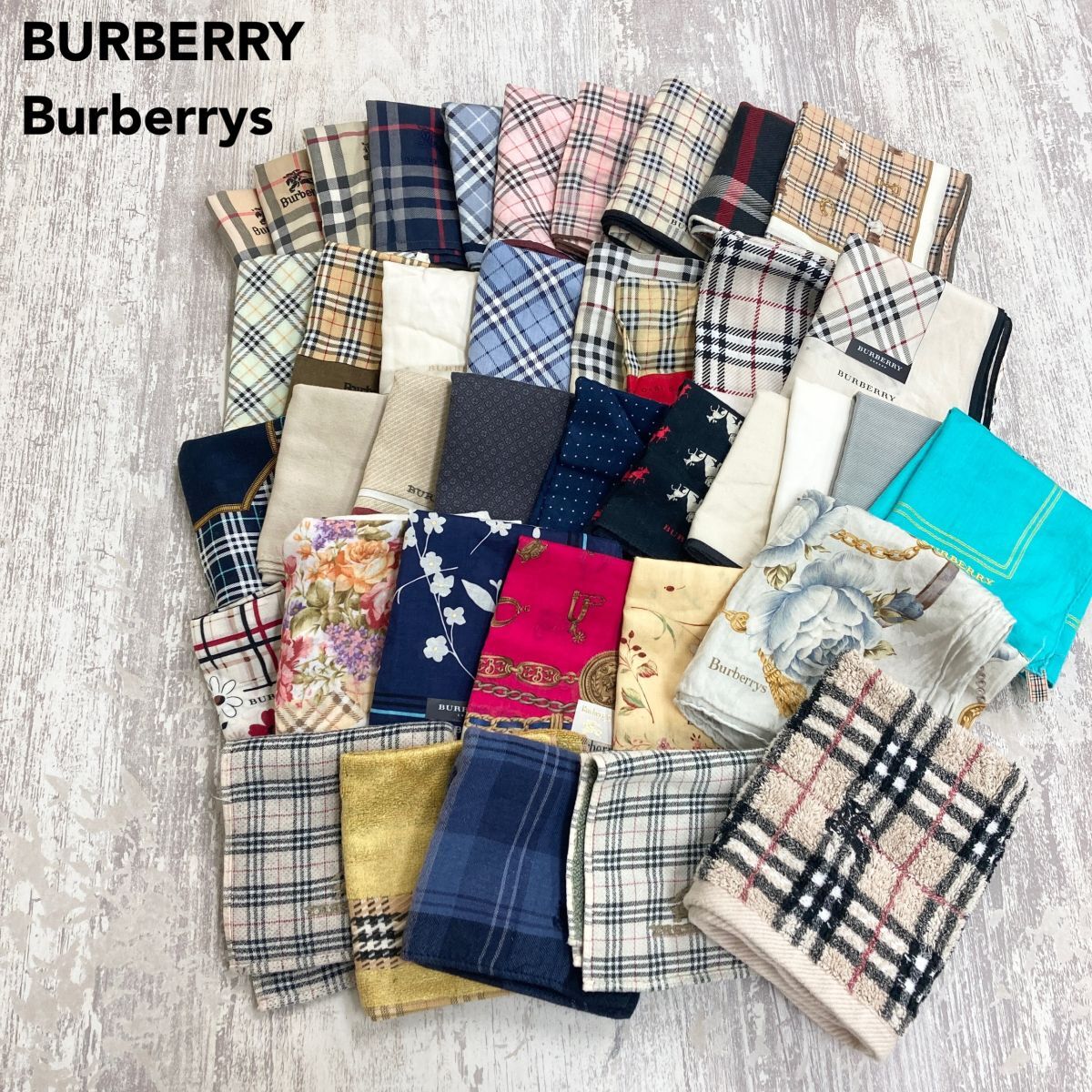 A spread of many Burberry-patterned handkerchiefs and mini towels arranged on a light wood floor.