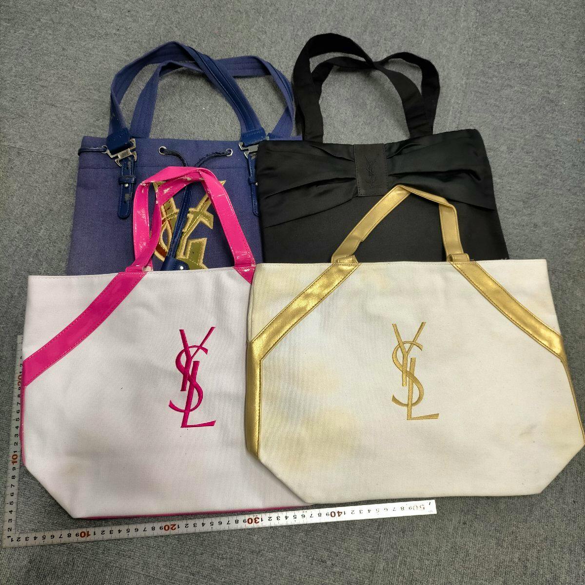 Four tote bags arranged on a gray surface (two white totes in front, a blue and a black bag behind) with a ruler at the bottom.