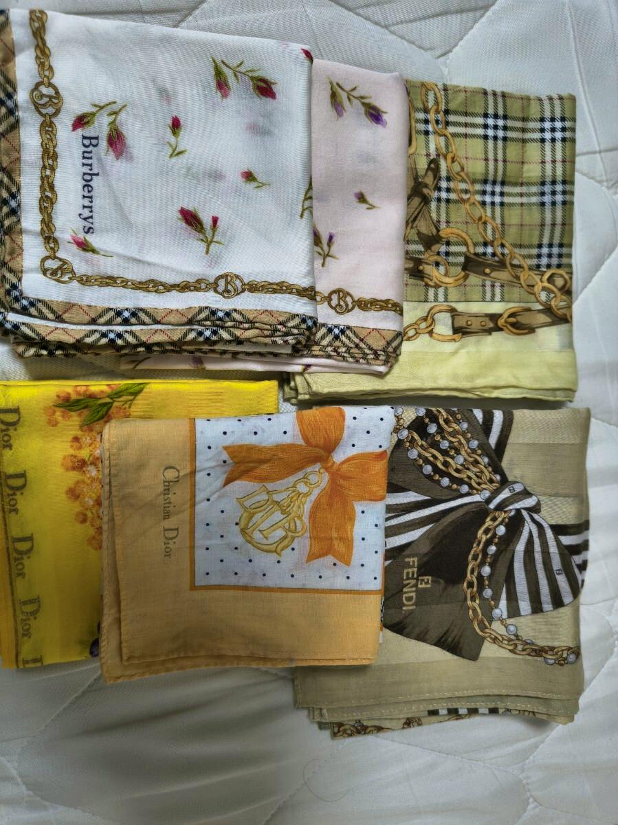 Folded branded handkerchiefs (Burberry, Dior, Fendi) stacked on a white quilted surface.