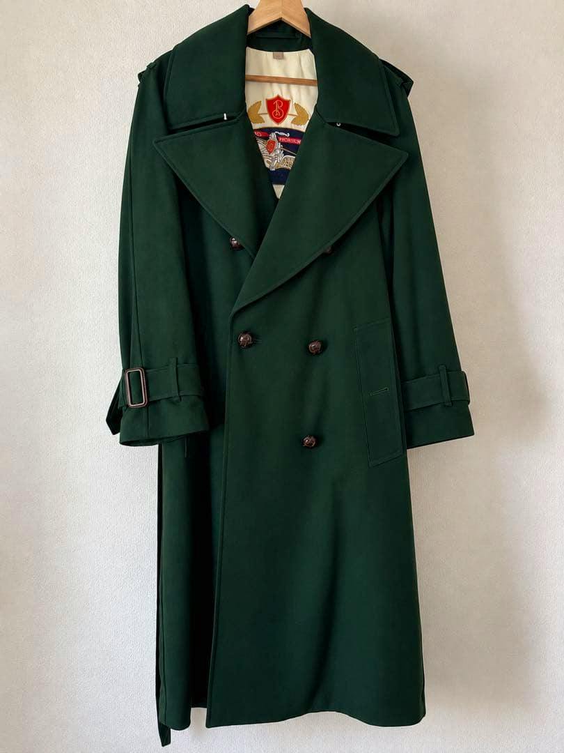 Green double-breasted Burberry wool long coat hanging on a wooden hanger against a plain wall.