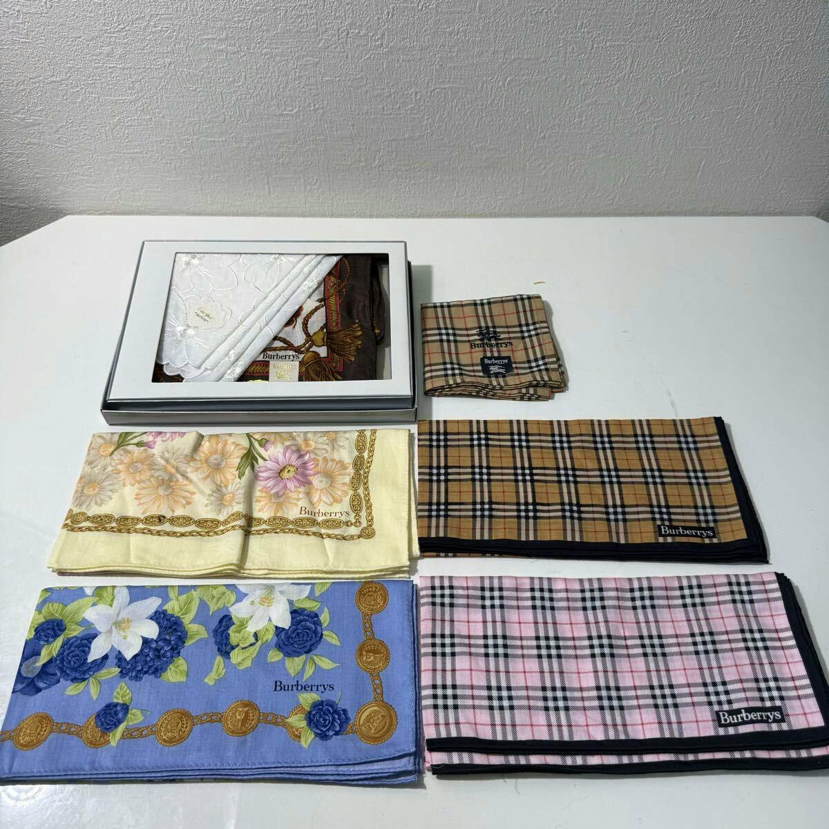 Six folded Burberry handkerchiefs, including classic check and floral designs, arranged on a white tabletop with a presentation box.