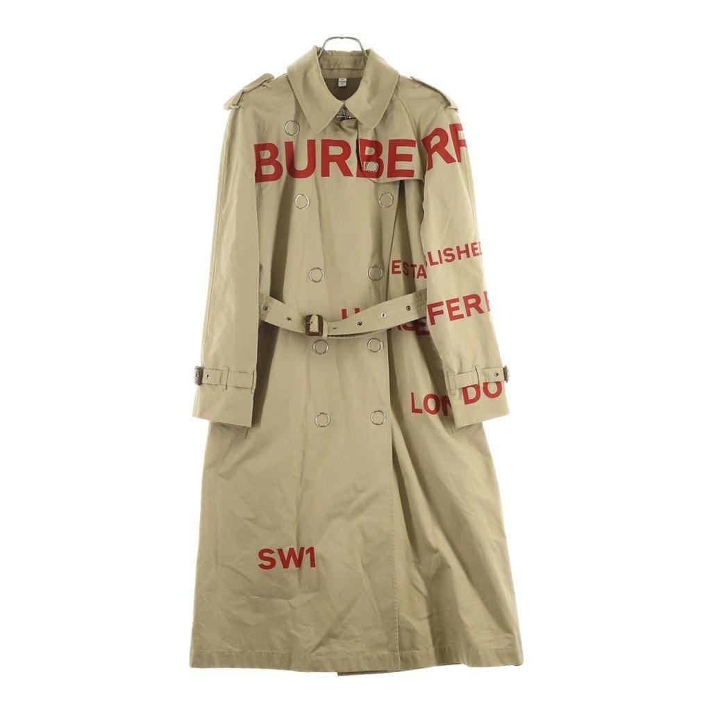 Front view of a beige BURBERRY women's trench coat with red printed lettering hanging on a hanger.