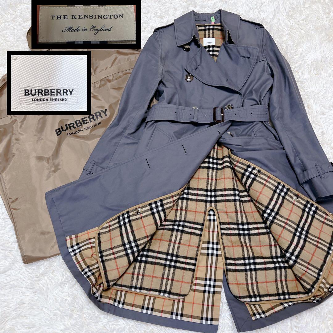Gray Burberry Kensington women's trench coat laid flat, opened to show the beige check liner and belt, with label insets and dust bag visible.