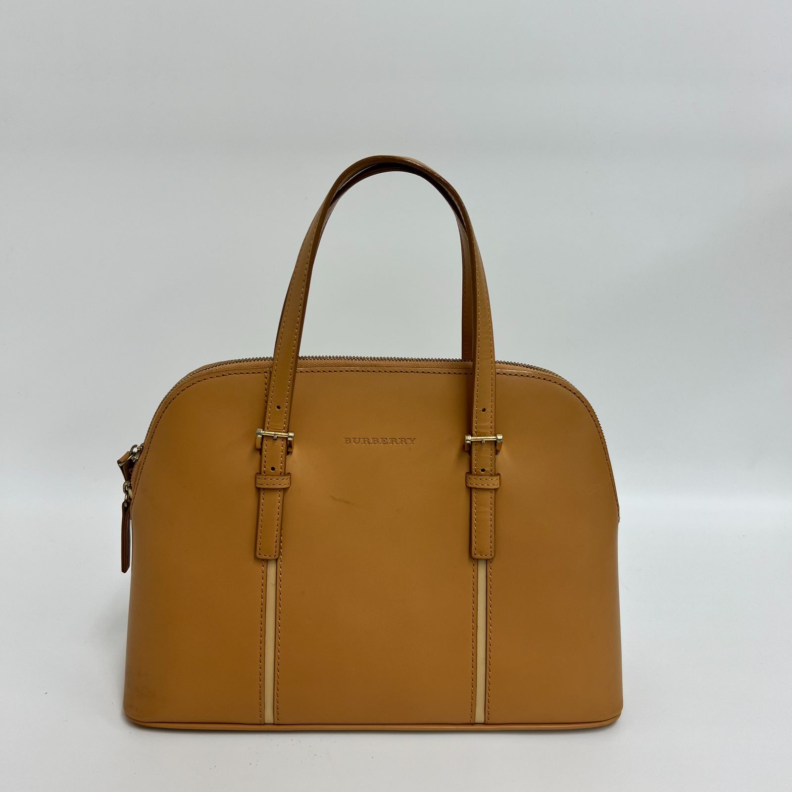 Front view of a camel-colored Burberry leather dome-shaped handbag with two top handles on a white background.