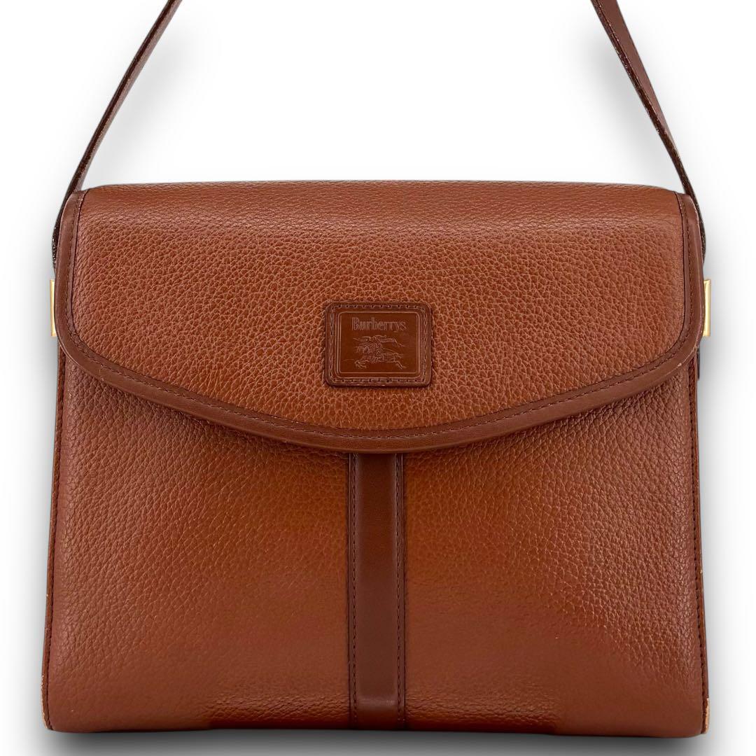 Front view of a brown Burberry leather shoulder bag with a flap closure and a centered horse‑logo leather patch.