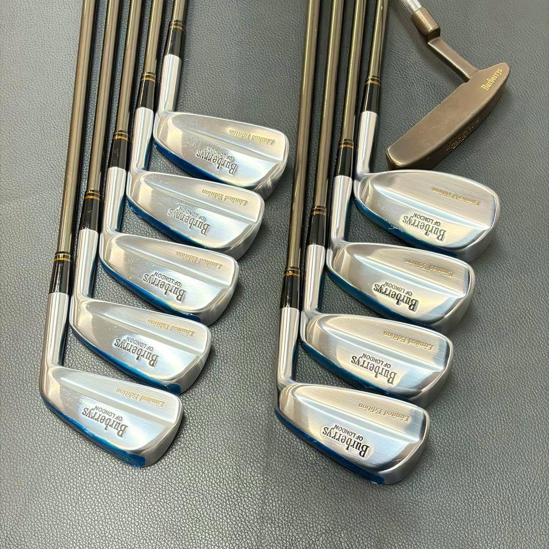 A set of Burberry limited edition golf irons and a putter laid out on a dark surface, showing the club heads.