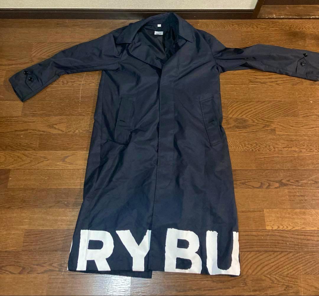 Black Burberry long coat laid flat showing the front with collar, long sleeves, welt pockets, and large white logo letters along the hem.
