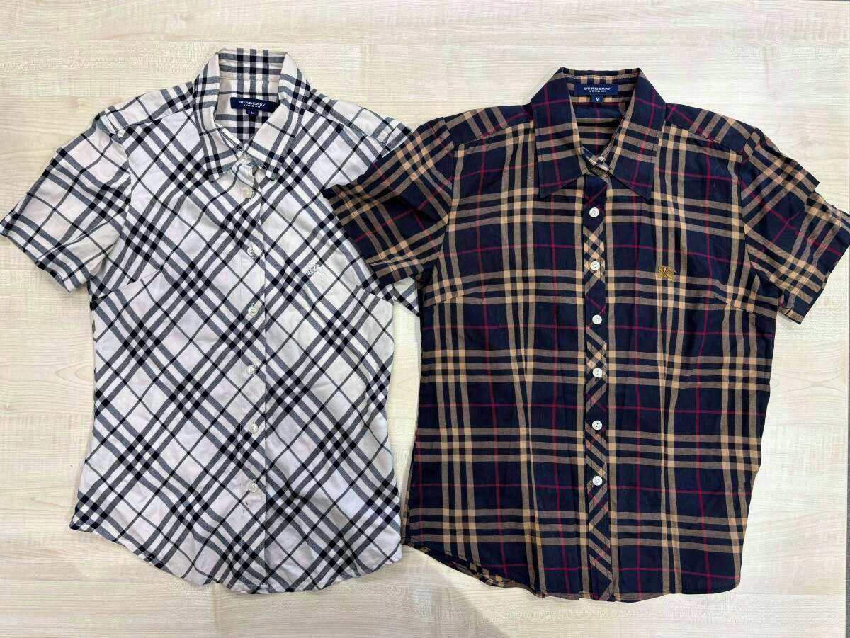 Two short-sleeve Burberry Nova check shirts laid flat on a light wood surface, one white/black check and one navy/tan check.