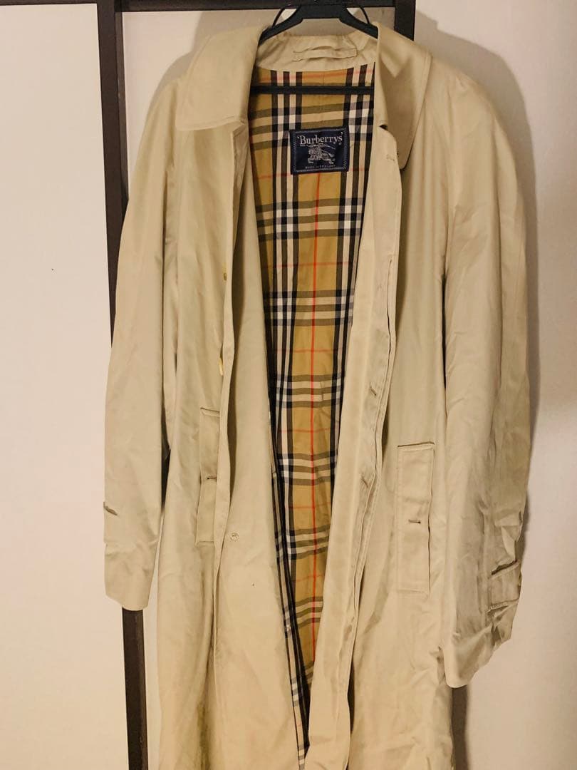 Beige Burberry men's stand-collar coat with visible Nova Check lining hanging on a hanger.