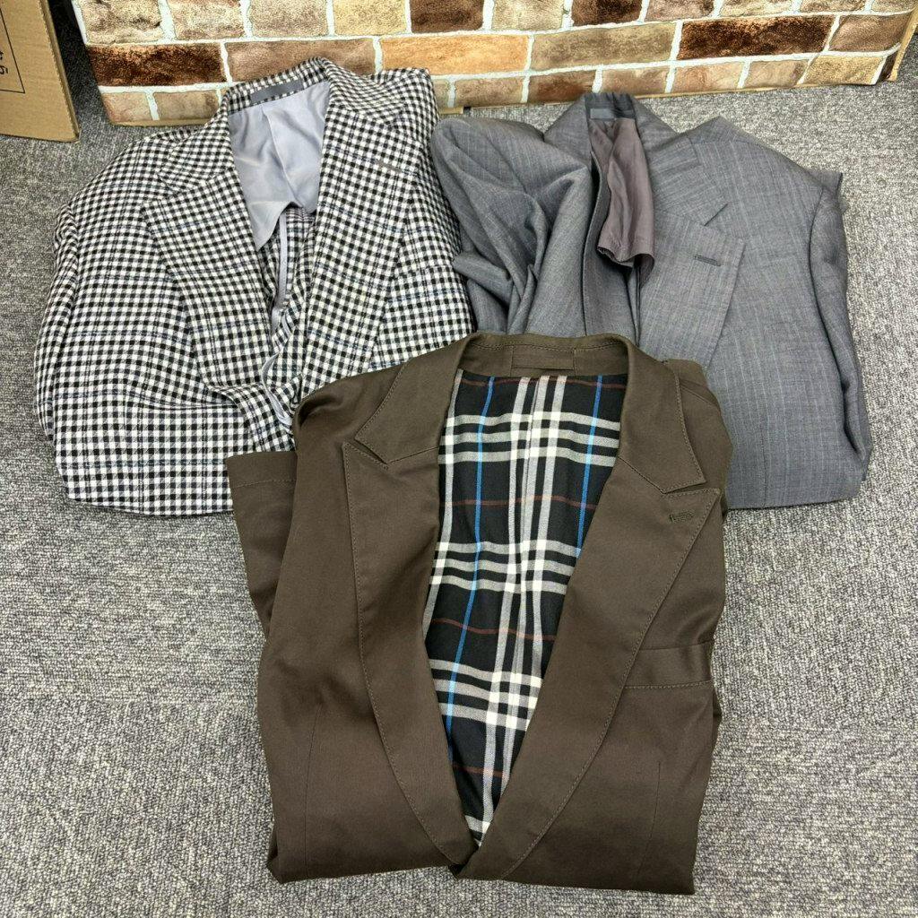 Three men's jackets laid flat on a carpeted floor: a black-and-white checked jacket, a gray jacket, and a brown jacket with a visible check-pattern lining.