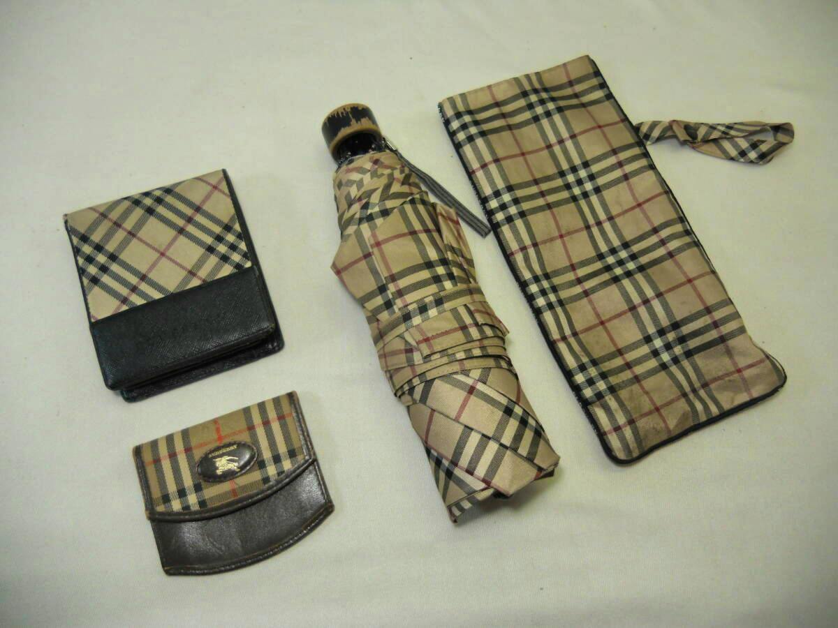 Folded Burberry check-pattern umbrella with matching pouch, a bi-fold wallet, and a coin purse laid on a white background.