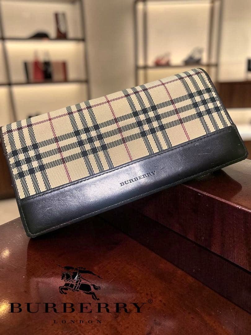 Burberry long wallet in beige Nova Check canvas with dark leather trim angled on a wooden surface.