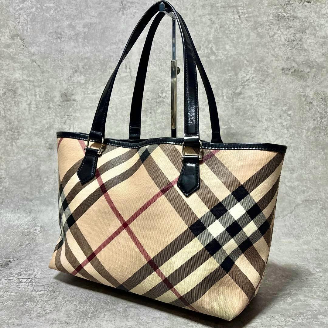 Burberry Nova Check mega-check tote bag in beige PVC with black handles photographed on a gray background.
