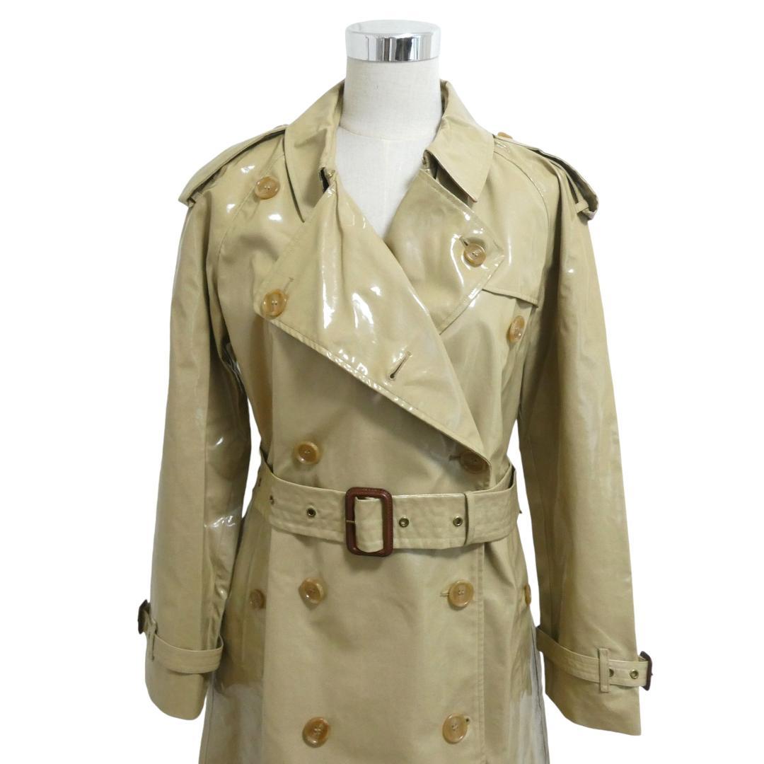 Front view of a beige patent PVC Burberry long trench coat with double-breasted buttons and a matching belt on a dress form.