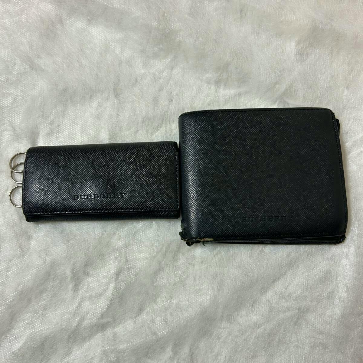Closed black Burberry wallet and matching key case made of saffiano leather on a light textured surface.