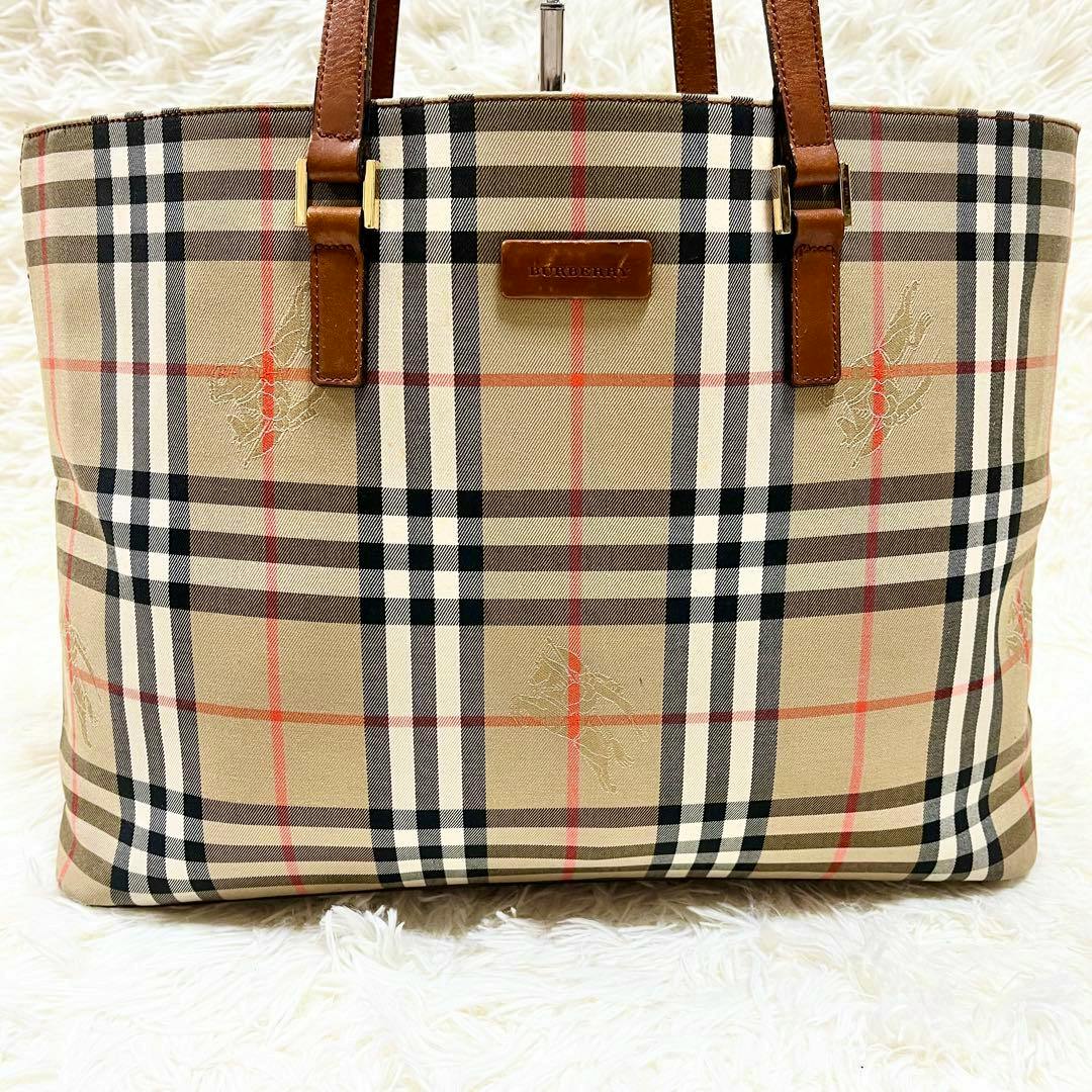 Front view of a Burberry Nova Check canvas tote bag with leather straps on a white shag background.