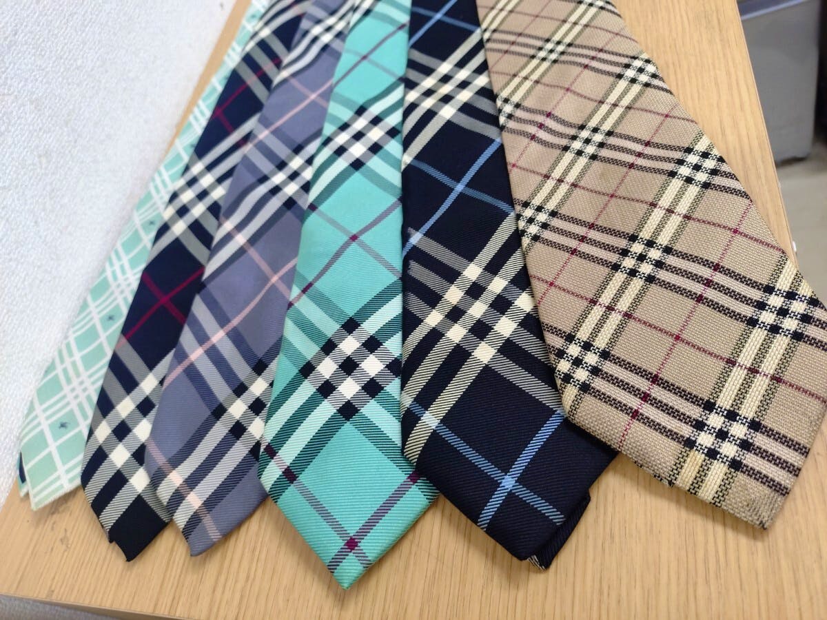 Six BURBERRY plaid silk neckties laid side by side on a wooden surface, showing various Nova Check patterns.