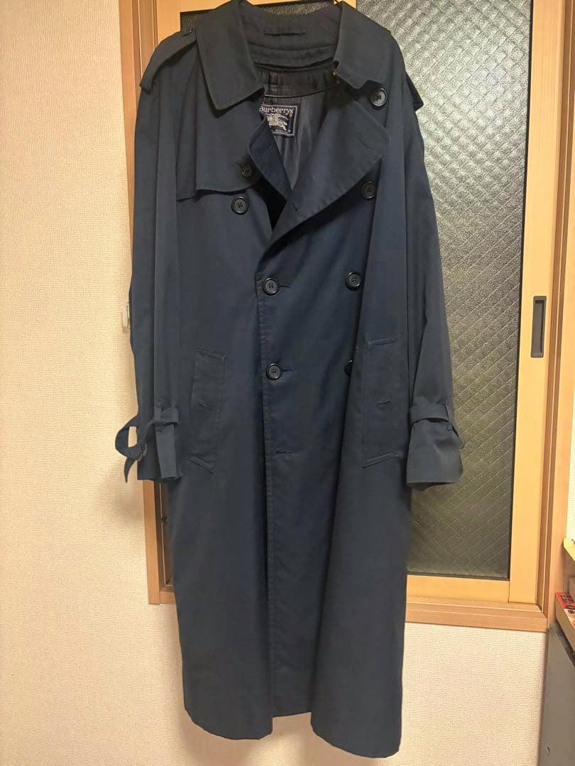 Front view of the navy Burberry trench coat hanging on a hanger, showing buttons, belt, and label.