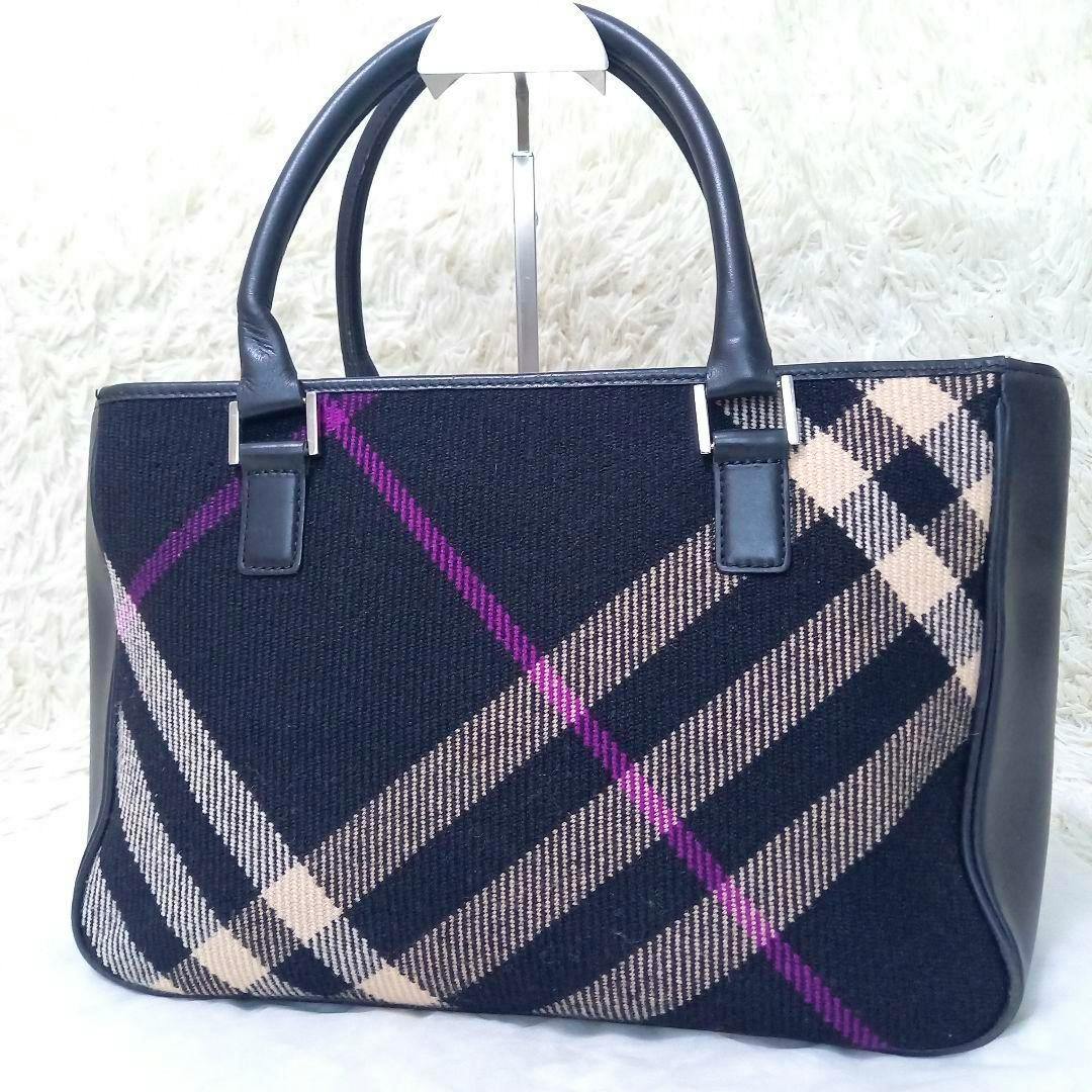 Front view of a Burberry tweed wool check tote handbag with black handles and a black, beige, and purple plaid pattern.