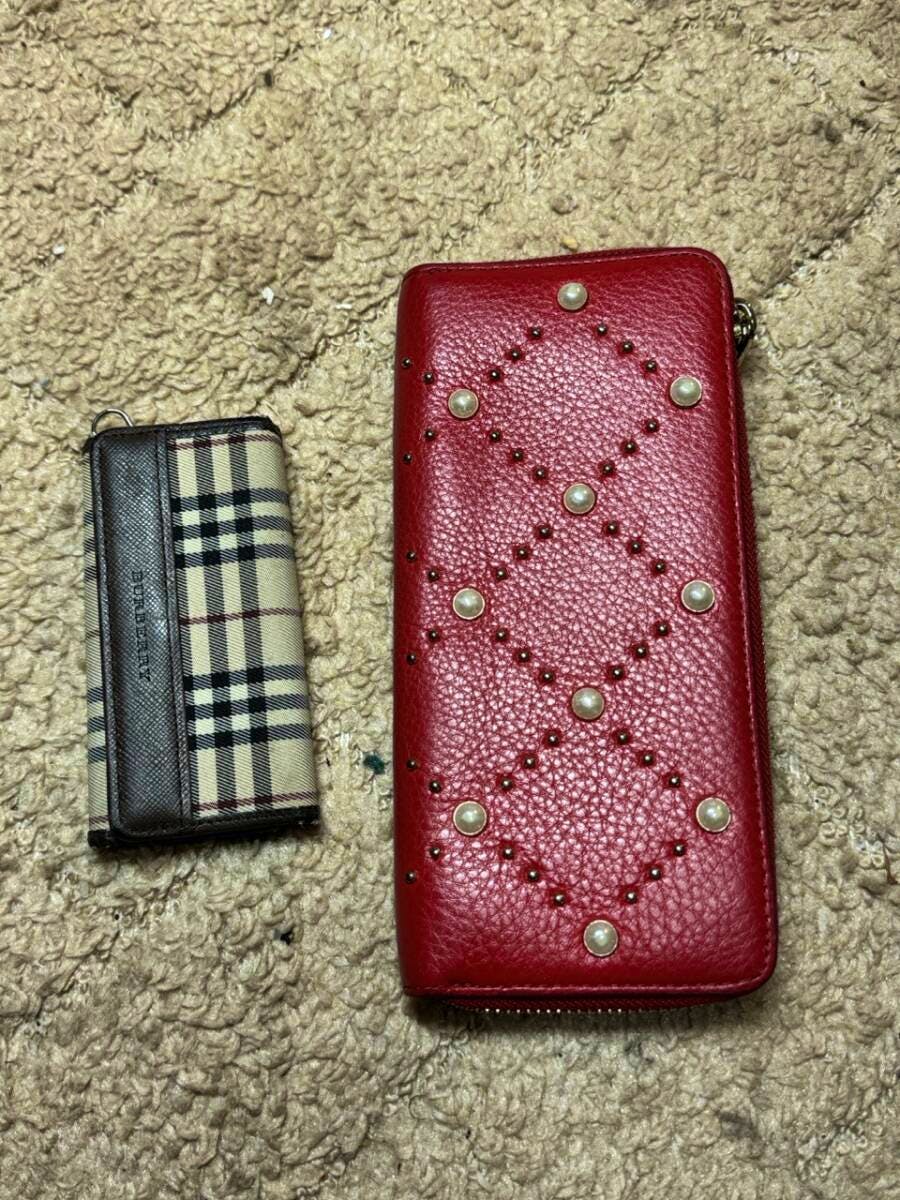 A Burberry keyring wallet in a beige check pattern next to a red Kate Spade long leather wallet with stud details on a carpet.
