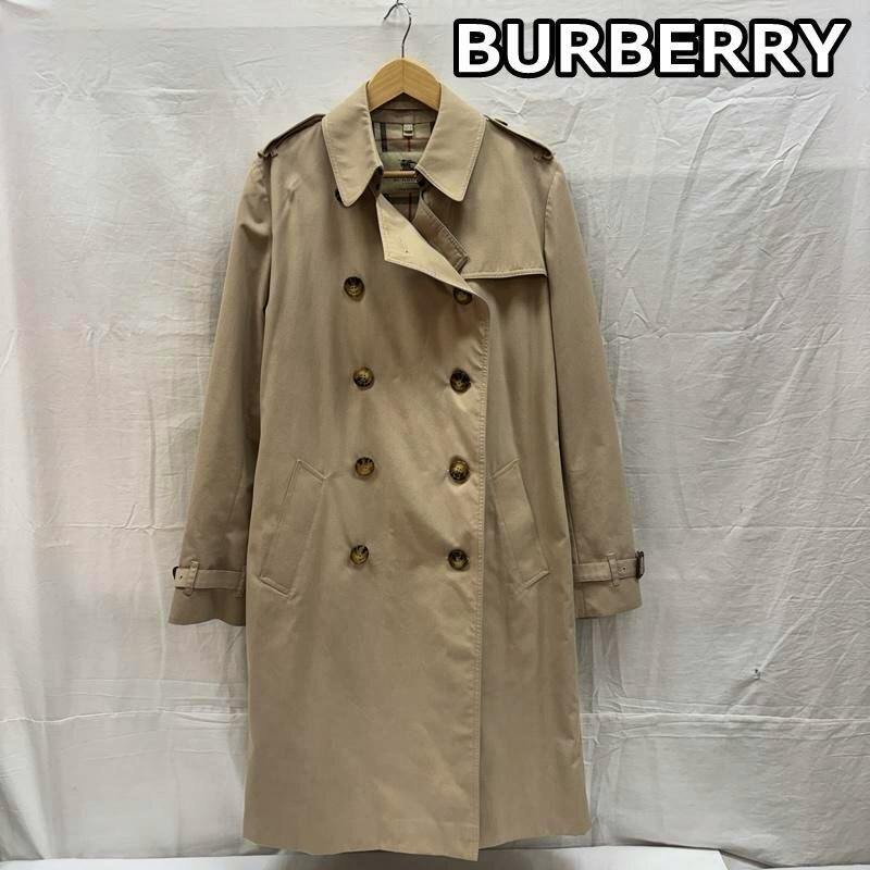 Beige long Burberry trench coat with double-breasted front hanging on a hanger against a white backdrop.