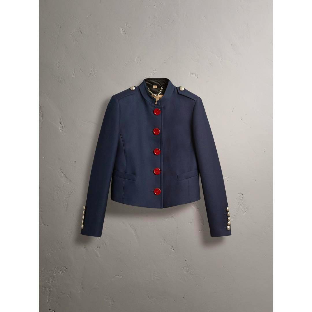 Navy Burberry collarless women's jacket with red buttons displayed against a gray wall.