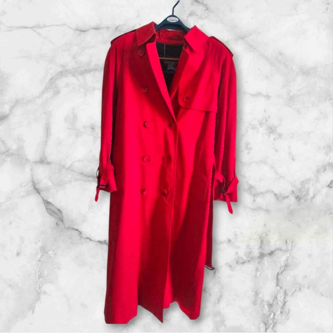 Front view of the red Burberry women's trench coat hanging on a hanger.
