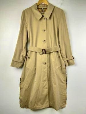 Beige Burberry women's side-slit trench coat hanging on a hanger against a white background.
