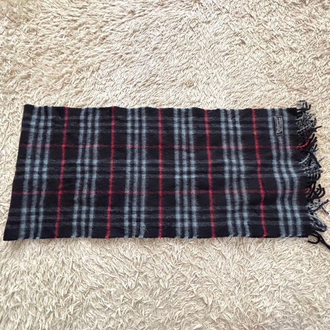 Burberrys cashmere check scarf in black, gray, and red with fringed ends laid flat to show full length.
