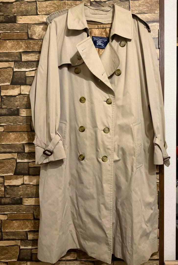 Front view of the Burberrys trench coat hanging on a hanger, showing the double-breasted buttons and label.