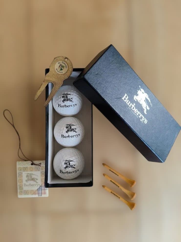 Three Burberrys golf balls in an open black Burberrys box with yellow tees, a divot tool, and a hang tag visible.