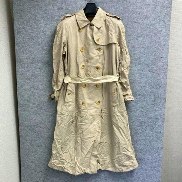 Beige double-breasted men's cotton trench coat with belt hanging on a hanger against a gray background.