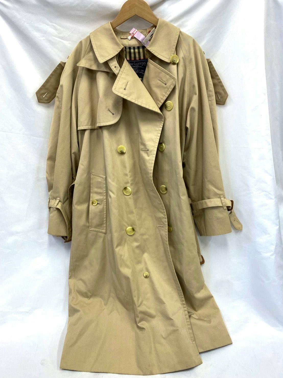 Beige Burberrys long men's trench coat hanging on a wooden hanger against a white backdrop.