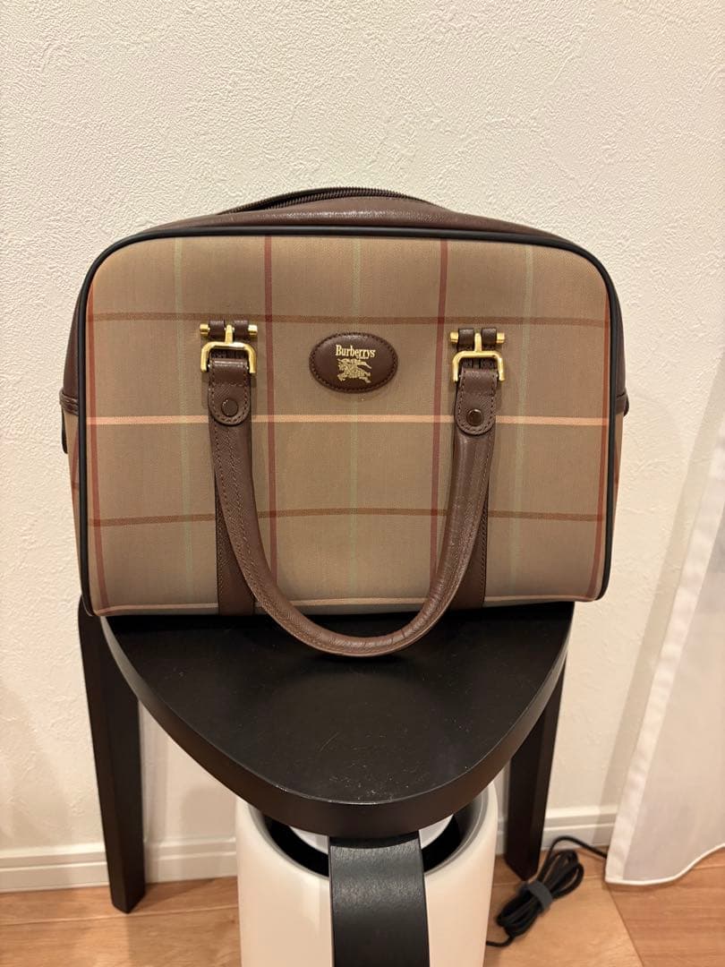 Front view of a brown Burberrys Nova Check canvas handbag with two top handles and a small oval logo plaque.