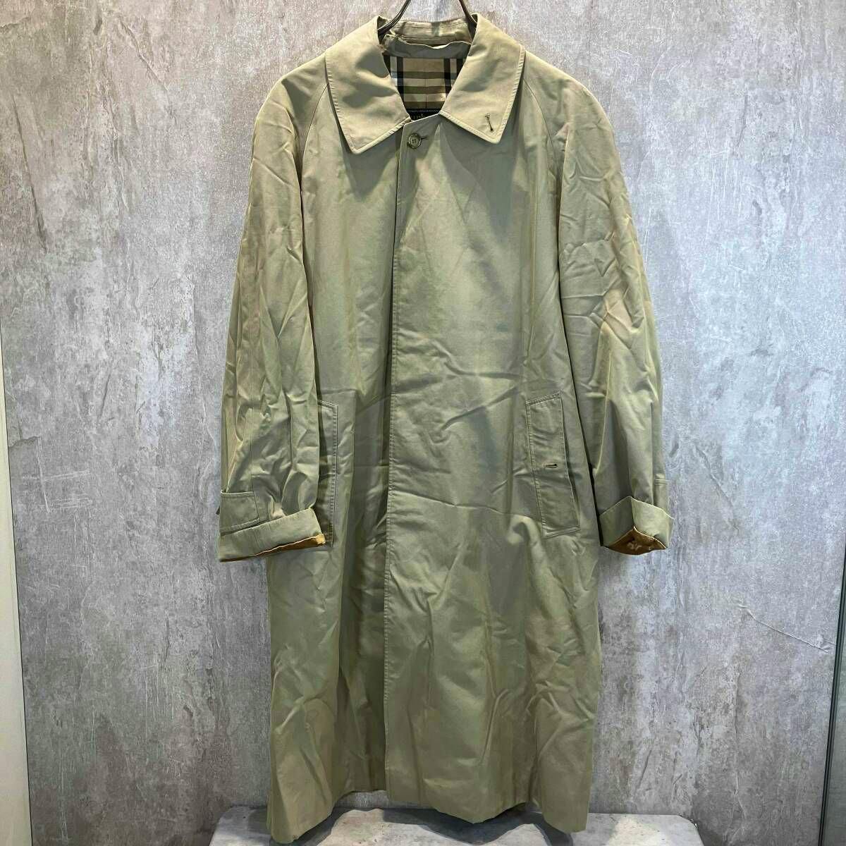 Beige Burberrys women's cotton coat hanging on a hanger against a grey textured wall.