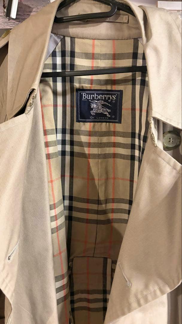 Interior of a women's Burberrys trench coat on a hanger showing the beige Nova check lining and part of the tan cotton outer.
