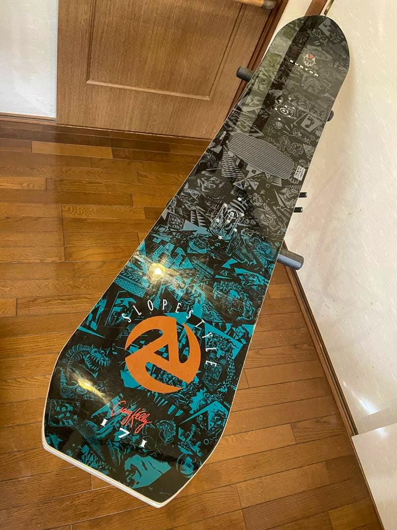 Top view of a Burton Kelly Air SLOPESTYLE snowboard showing its blue and orange graphics on a wooden floor.