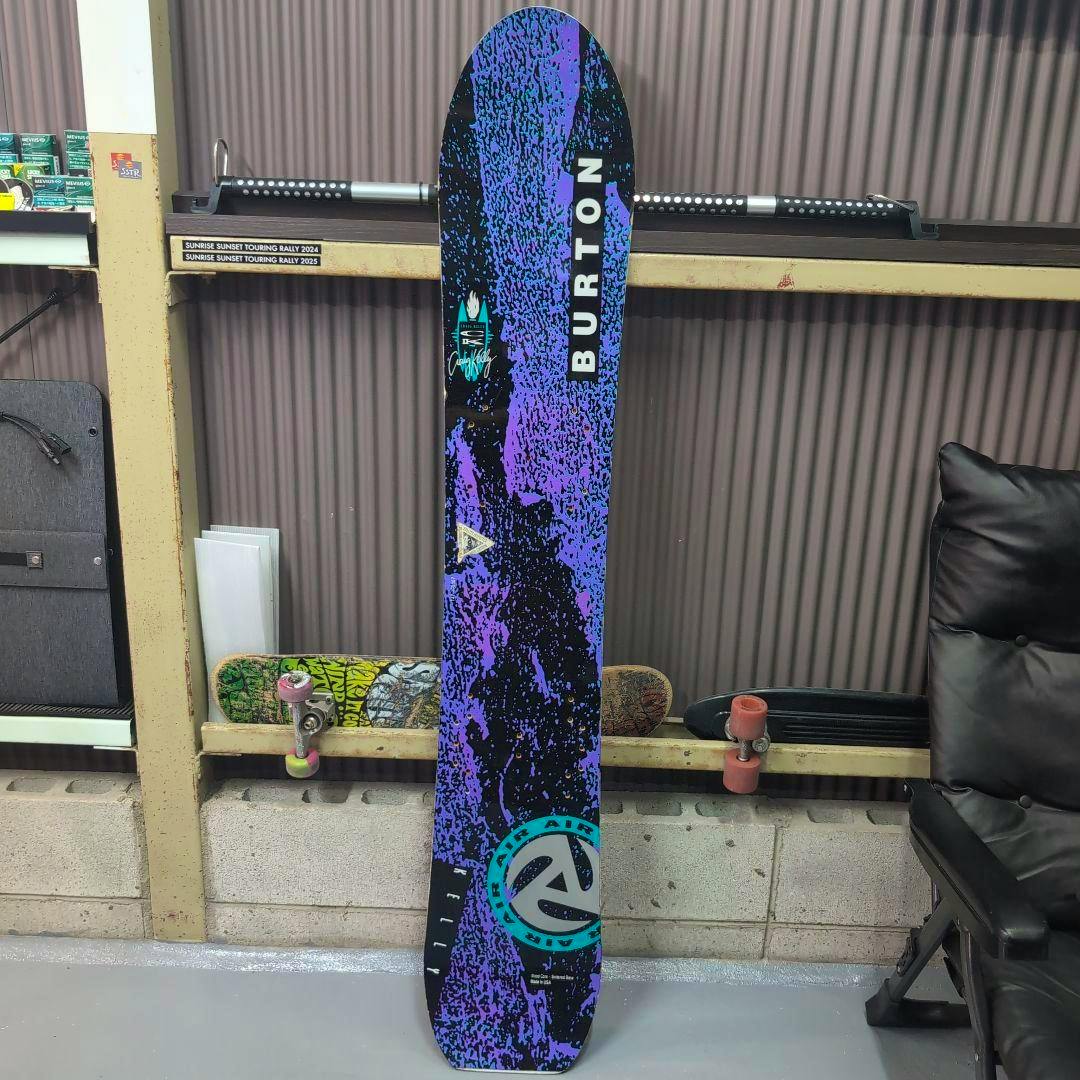 Vintage Burton Kelly Air snowboard standing upright showing a purple-and-black splatter top graphic with a vertical BURTON logo.