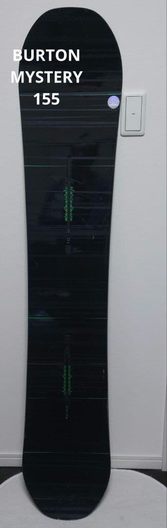 A black Burton Mystery 155 snowboard photographed upright against a white wall.